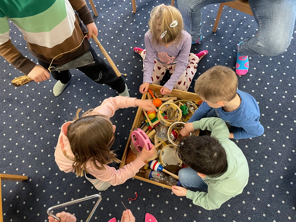 Die Kinder wühlen in einer großen Kiste mit vielen kindgerechten Instrumenten.