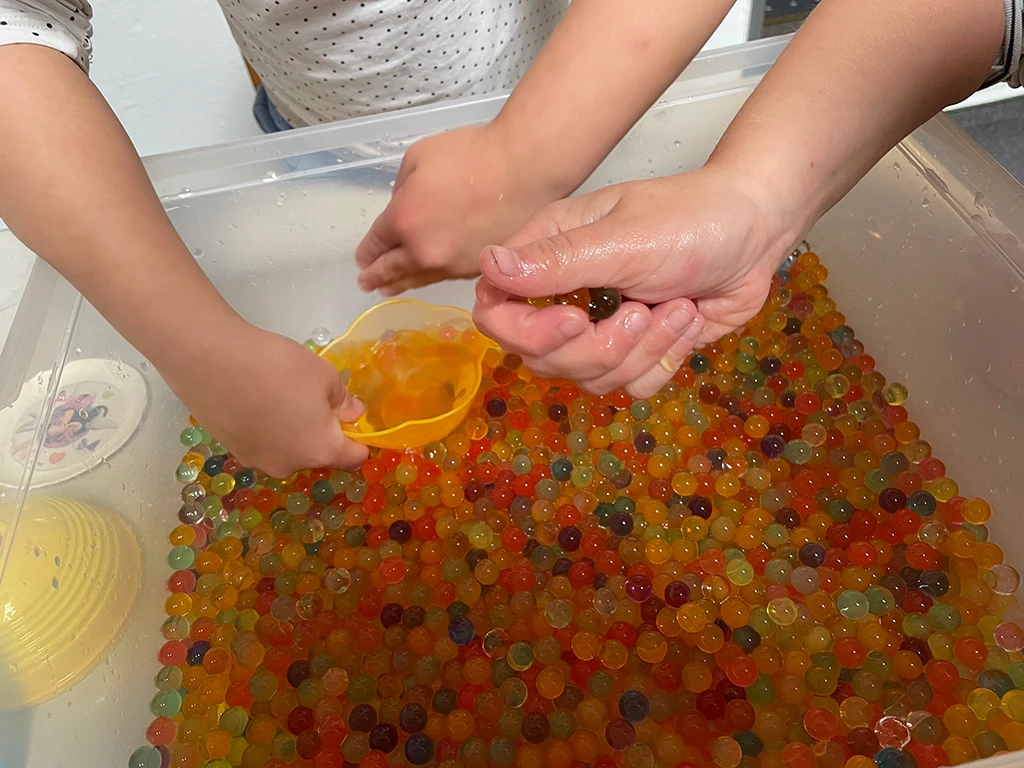 Kinderhände in einer Schüssel voller bunter Kugeln.