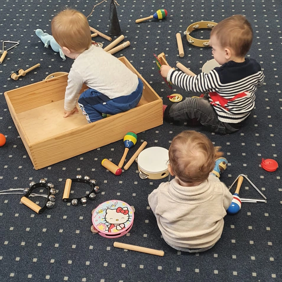 Die Kinder haben Klangstäbe, Triangeln Schellen, Rasseln und andere altersgerechte Musikinstrumente.