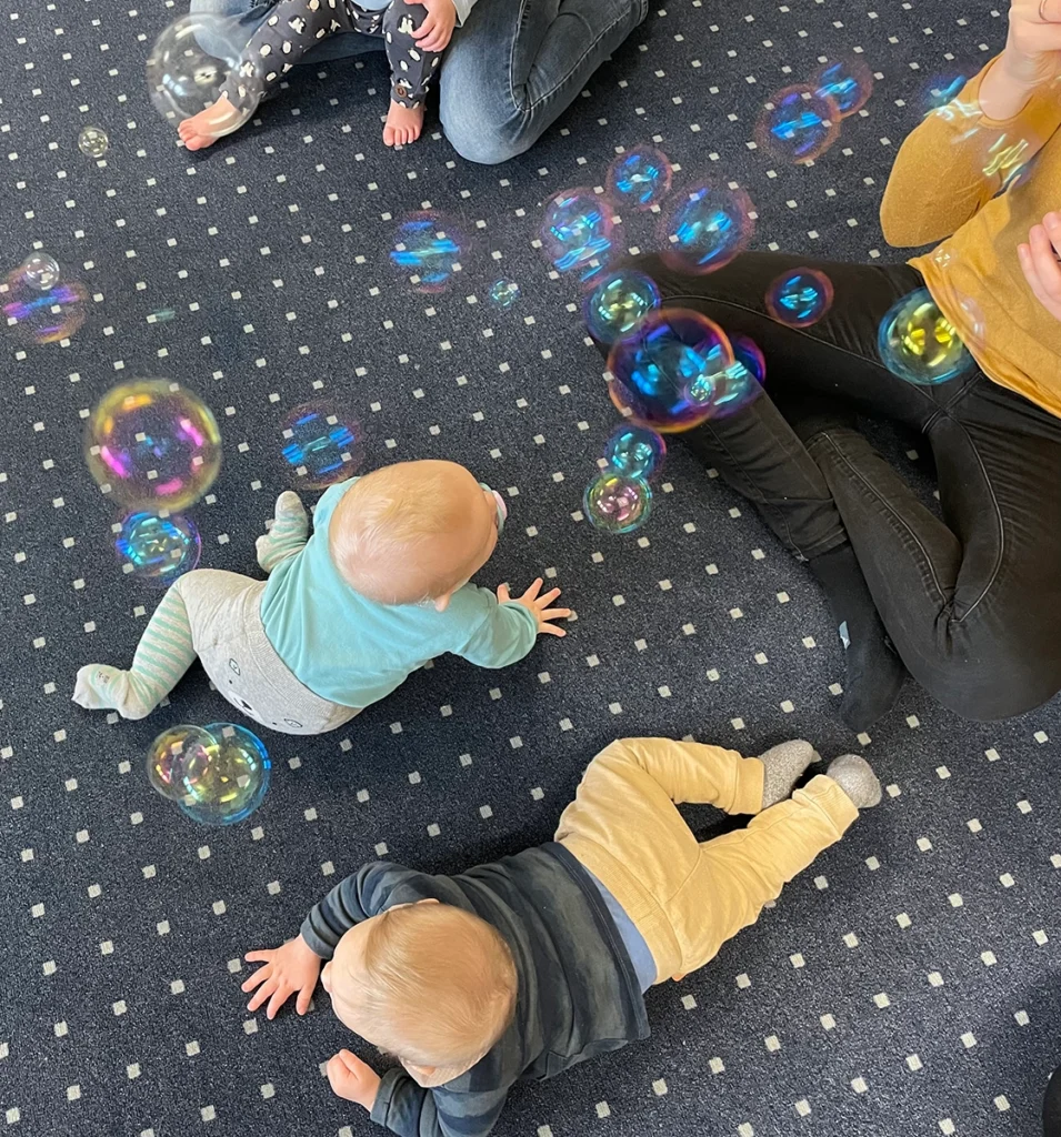 Babys krabbeln auf dem Teppich und wollen Seifenblasen fangen.