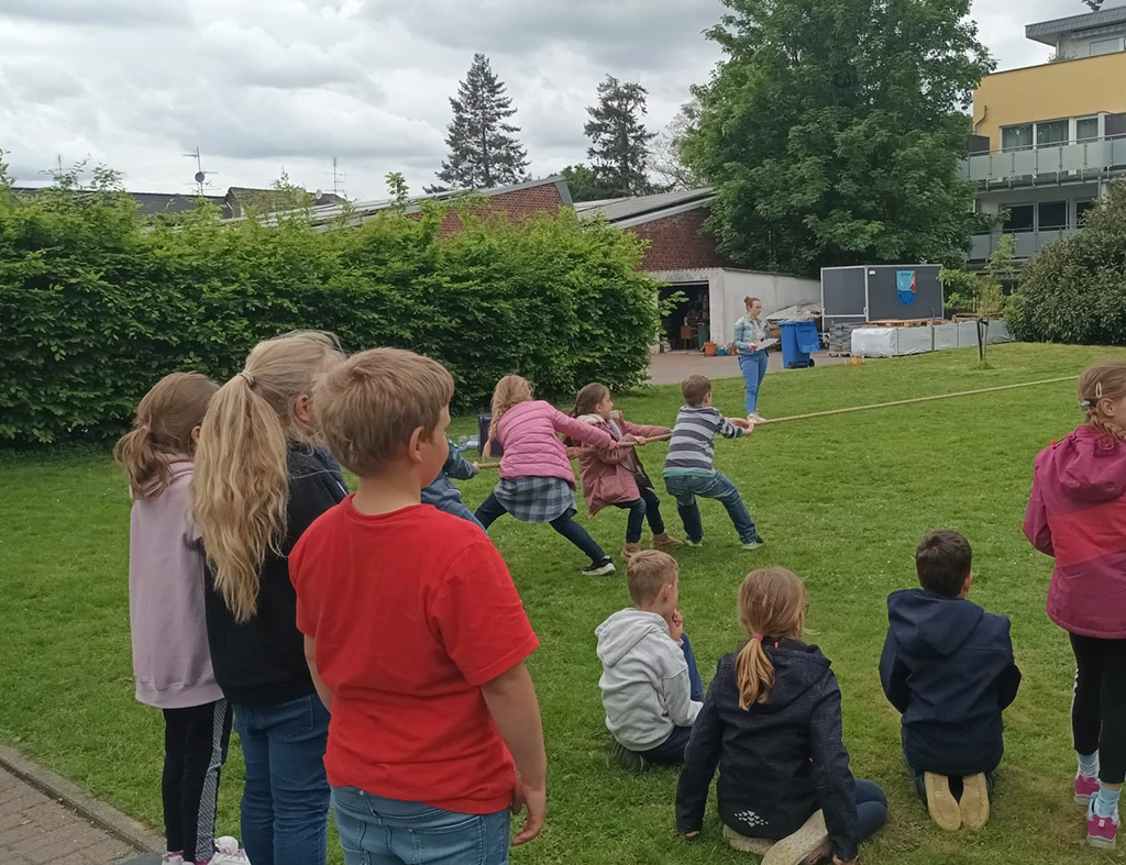 Kinder auf einer Wiese ziehen am Tau.