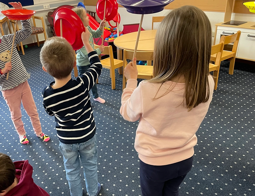 Die Kinder balancieren rote Teller auf Stangen