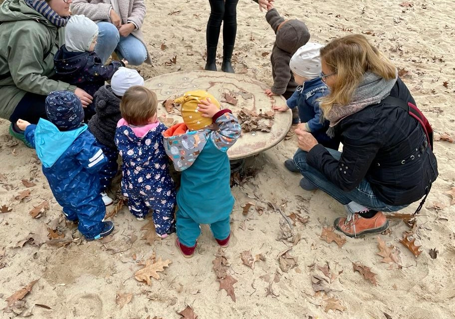 Kleine Kinder stehen im Sand um eine große Scheibe herum.