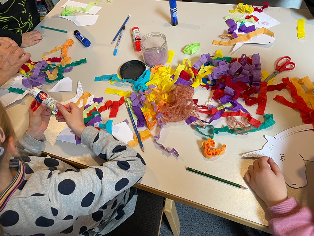 Kinder verzieren ausgeschnittene Formen mit Streifen aus Krepp.