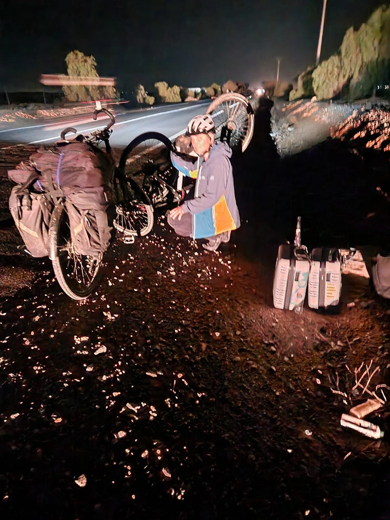 Christoph Roller hockt vor seinem defekten eBike im Dunkeln am Straßenrand hinter Settat. Hinter ihm seine beiden Koffer.