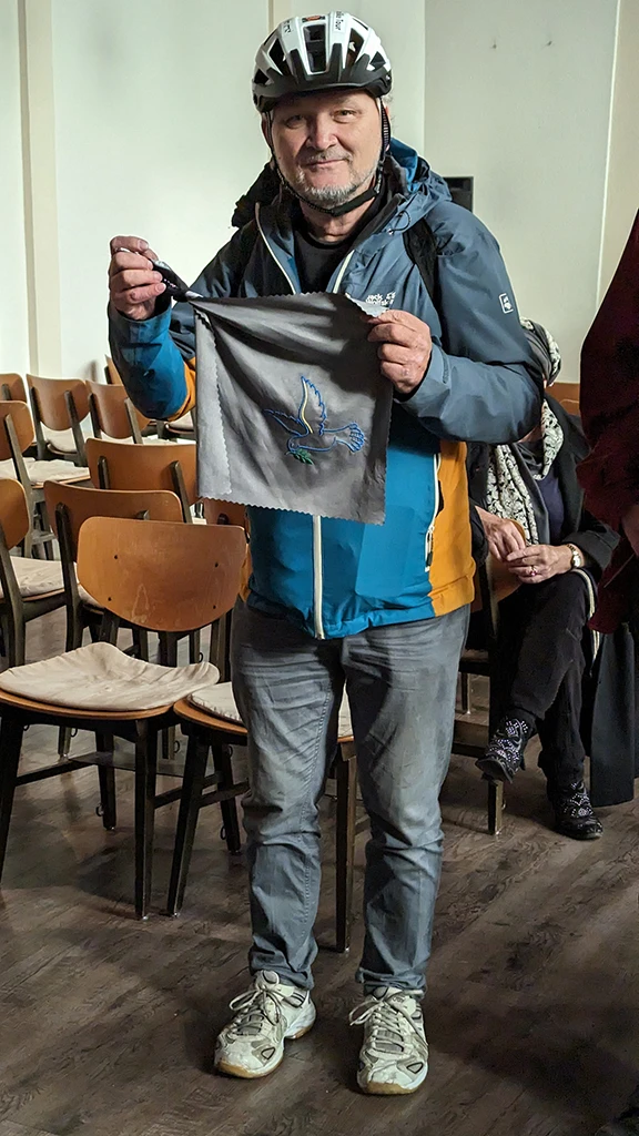 Christoph Roller hält ein Reisehandtuch in der Hand, auf dem eine Friedenstaube gestickt ist.
