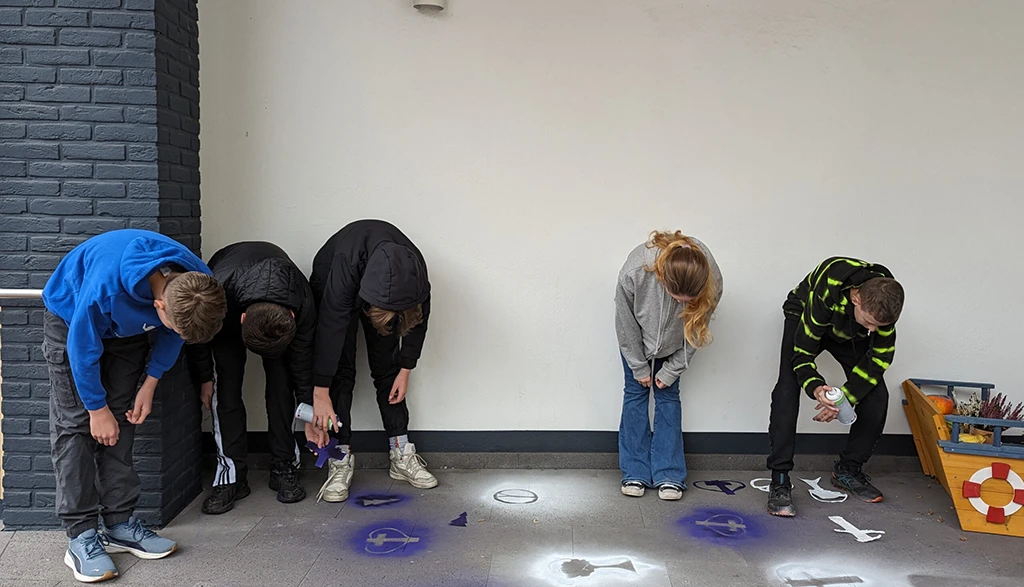 Fünf Konfirmanden schauen auf ihre auf den Boden gesprühten Friedenstauben.