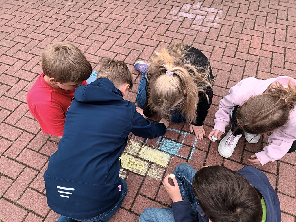 Kinder malen auf dem roten Pflaster mit blauer und gelber Kreide